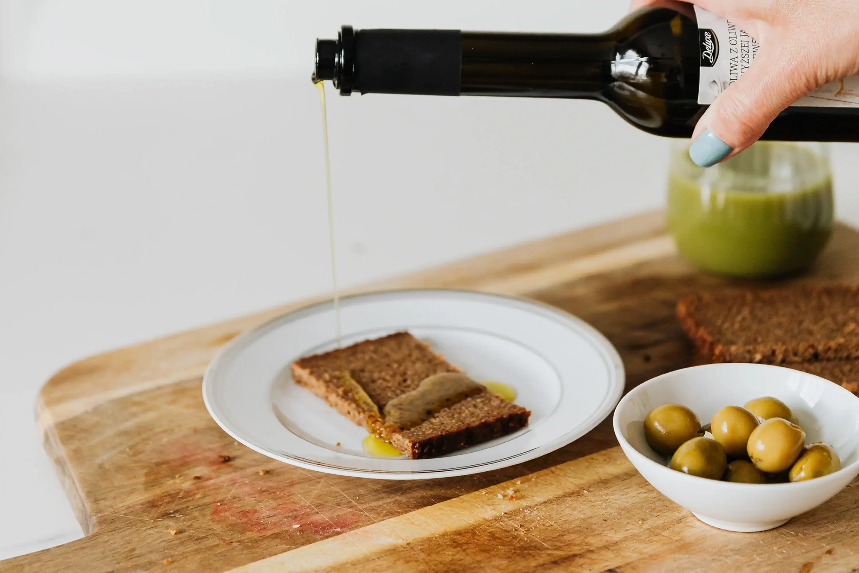 hand pouring olive oil out of a bottle onto a slice of bread